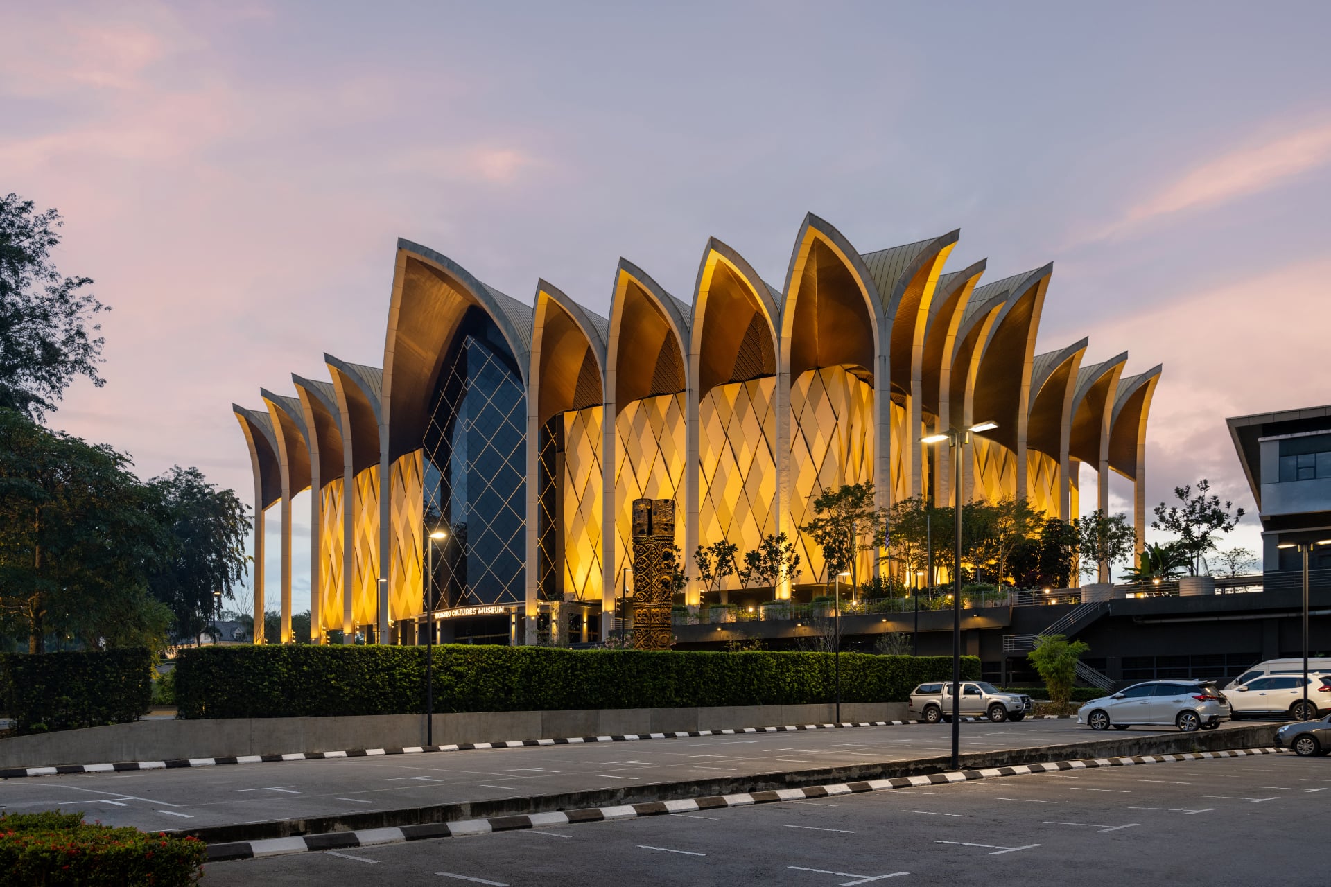Evening aerial view of the Borneo Cultures Museum in Malaysia with illuminated façade and atmospheric outdoor lighting.