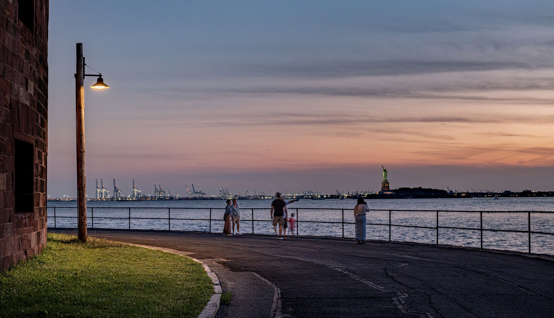 Waterfront promenade on Governors Island, New York, lit by a WE-EF pole-mounted luminaire, with the Statue of Liberty at sunset