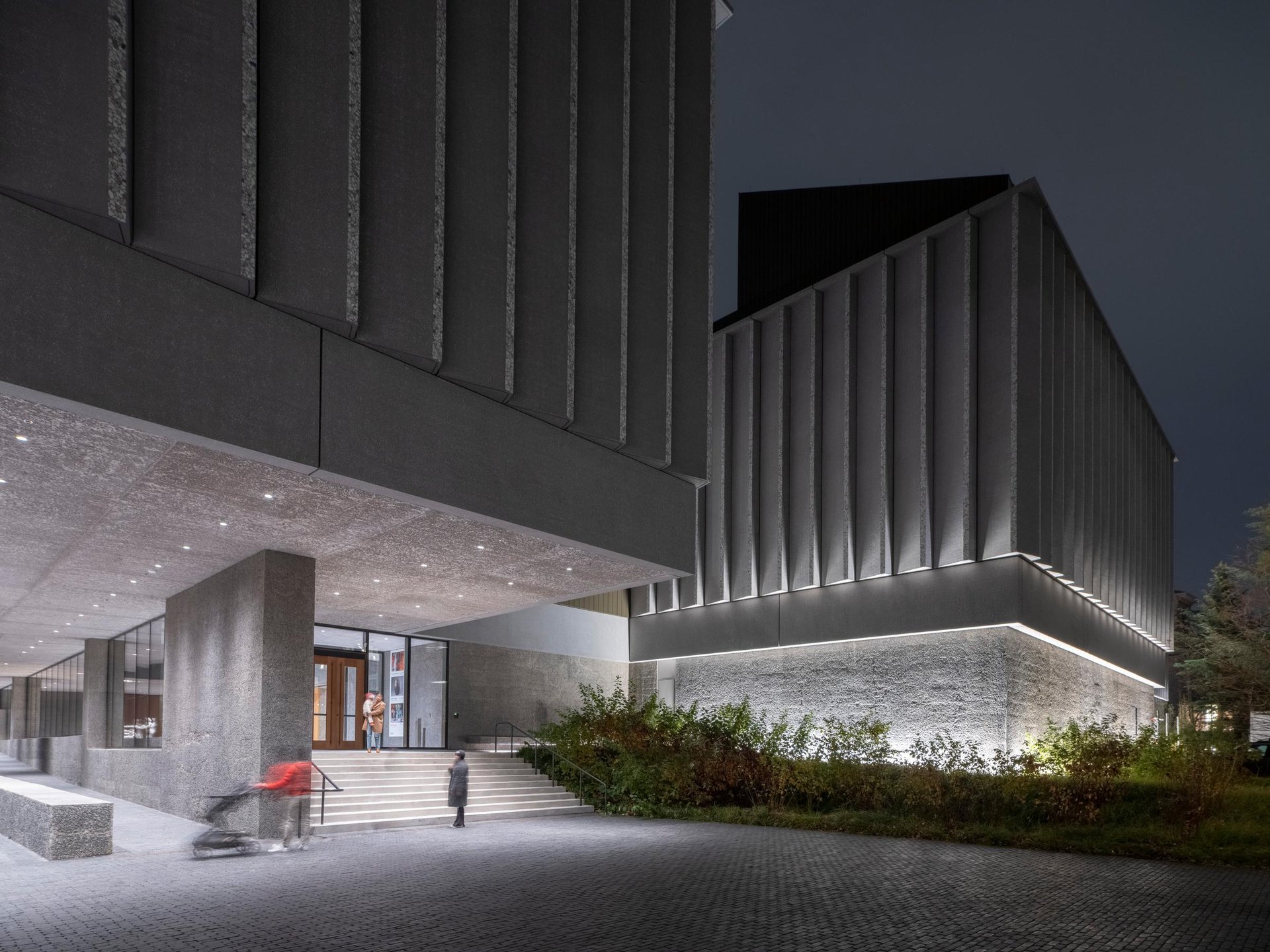 Front steps to museum, people walk up it, it is lit by downlights