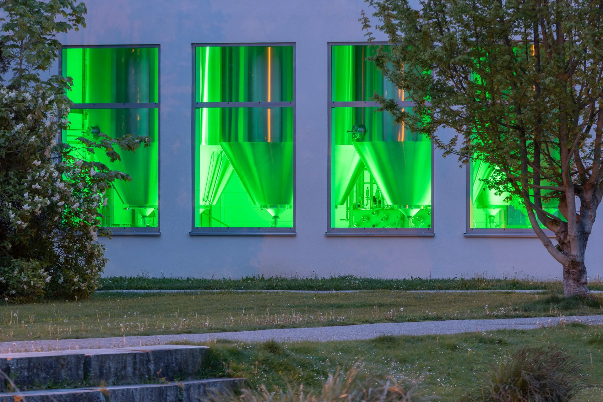 Schattenhofer Brewery fermentation tank building exterior showing multiple panoramic windows bathing gleaming stainless-steel fermentation tanks in saturated green light using six WE-EF FLC220-CC RGBW projectors controlled via DMX touch panel in anteroom, creating dynamic presentation visible through windows as local talking point and brewery tour attraction along popular Sulz river cycling route in small Bavarian town Beilngries