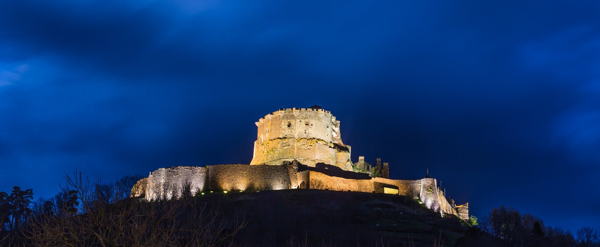 Le château de Murol en Auvergne, avec son donjon médiéval et ses remparts illuminés par des projecteurs au sommet d'une colline, de nuit