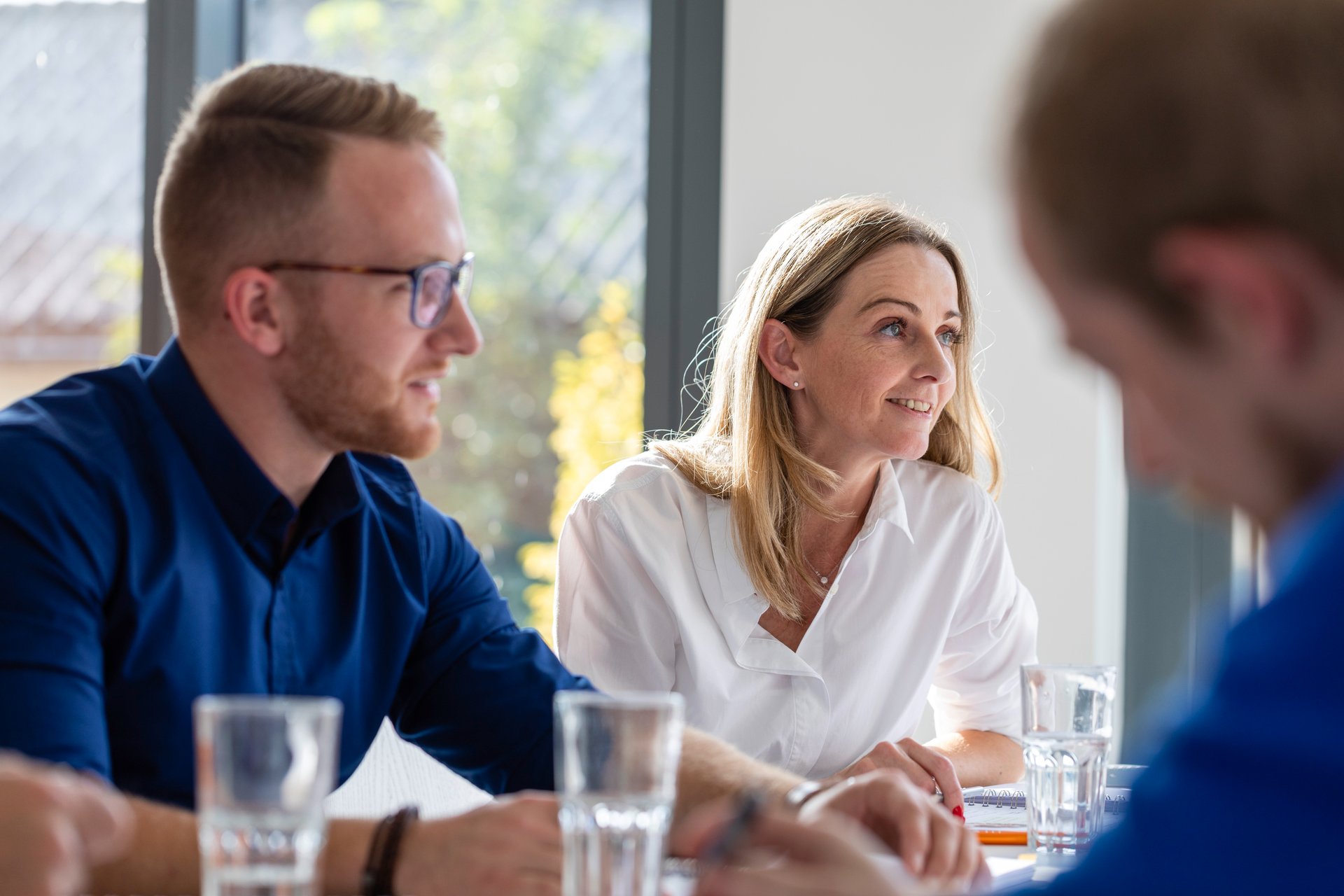 WE-EF colleagues listening attentively during a team meeting around a table with water glasses in a bright office