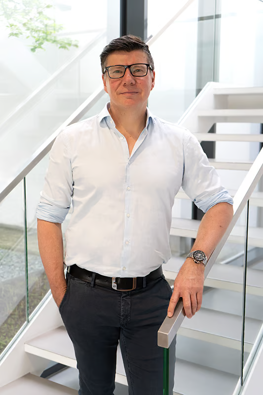 Porträt von Robert Diedrich, Global Head of Marketing der WE-EF Group, der an einem Handlauf einer Treppe im Hauptsitz des Unternehmens lehnt.