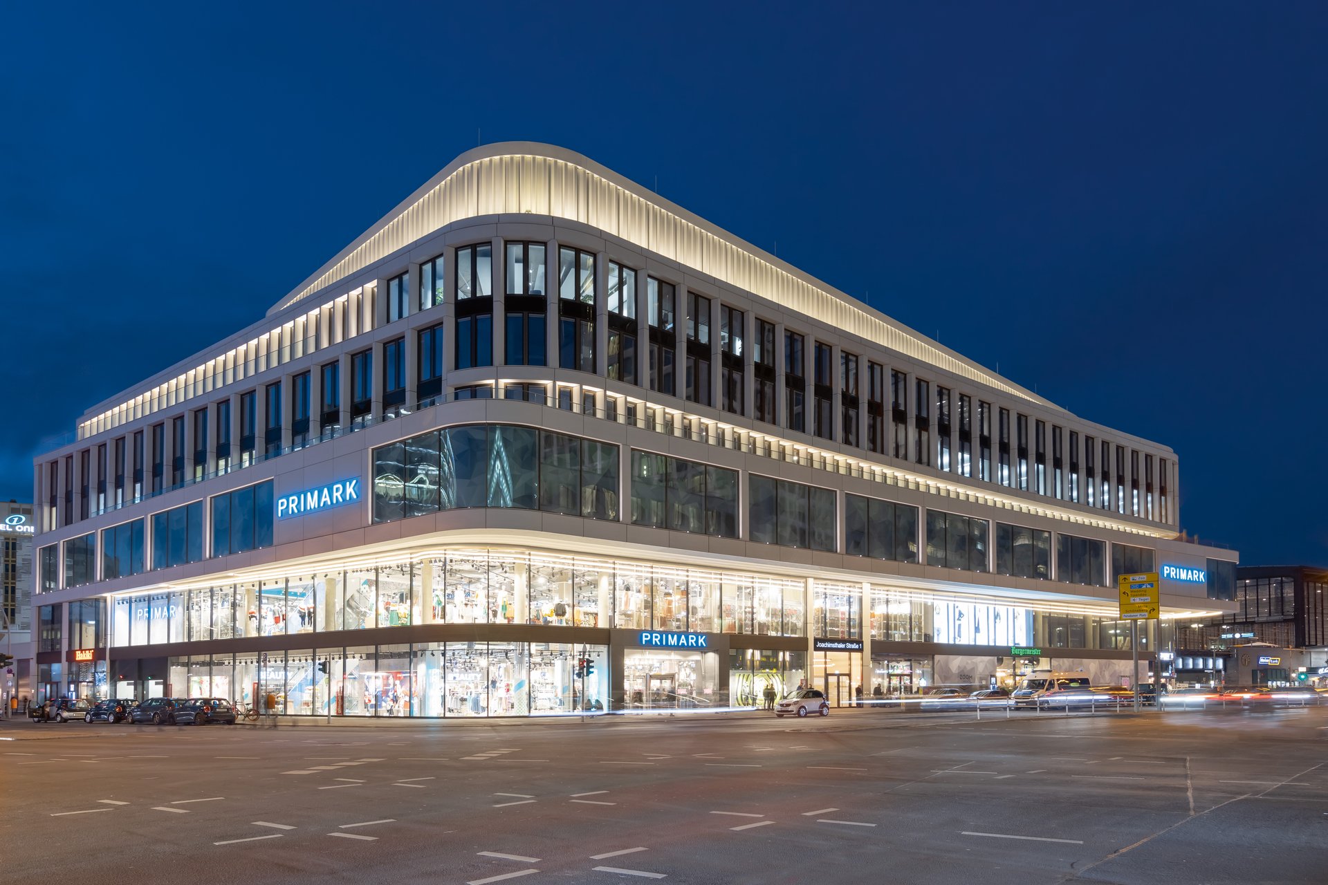 Zoom office building Berlin illuminated at night with WE-EF FLC121 projectors creating bright roof crown and horizontal light bands near Zoo station