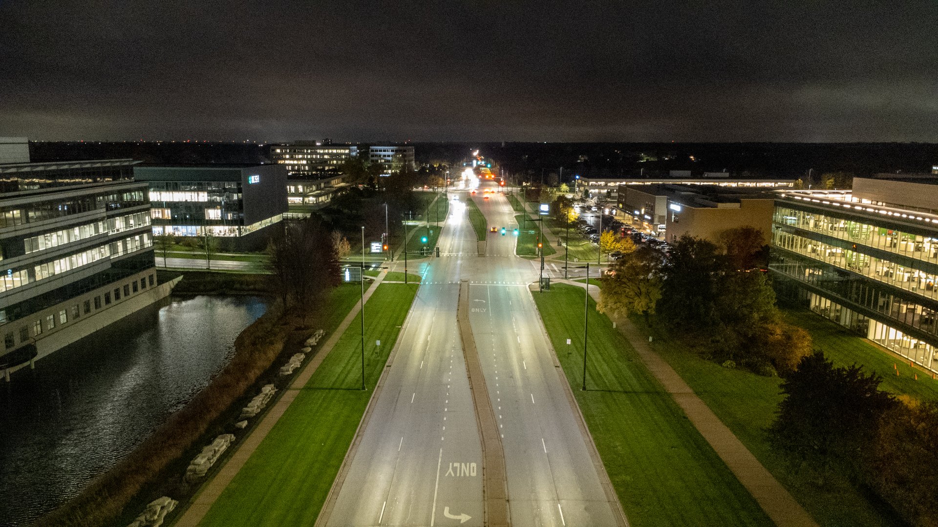 Roadway at night, there are cars at the intersection and tall street lights illuminating the roadway