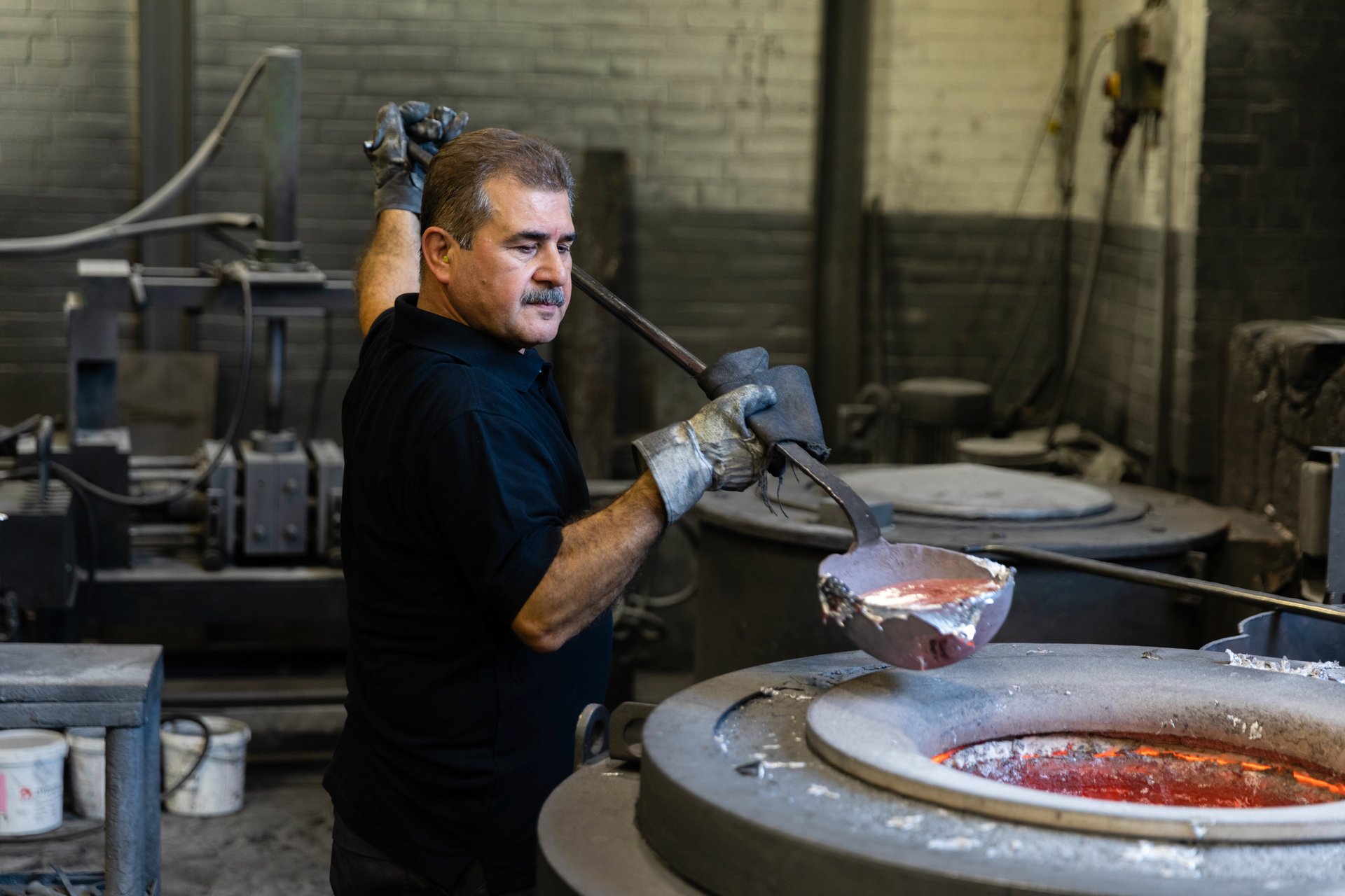 Worker at the WE-EF foundry ladling molten aluminium from the furnace during the production of luminaire components.