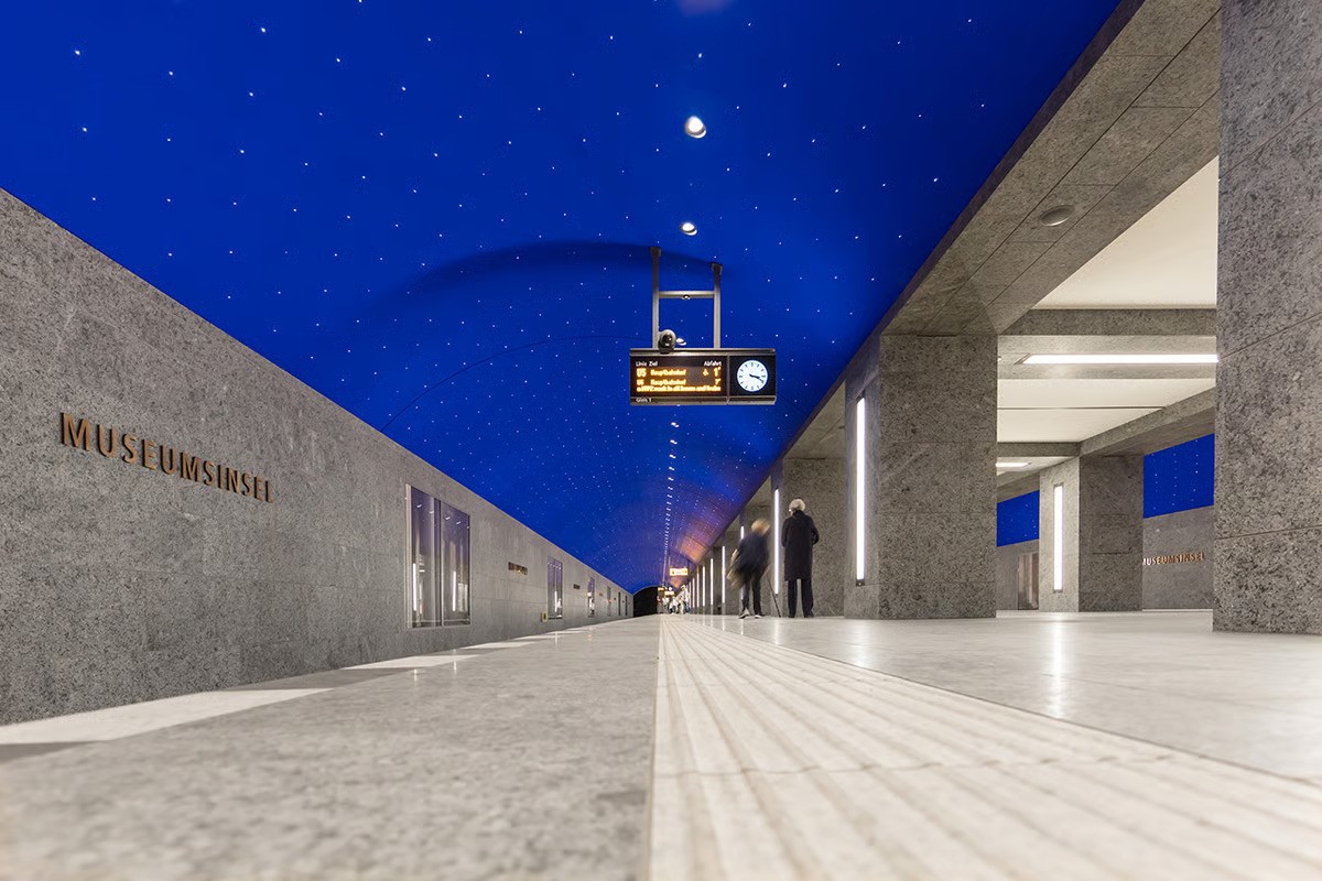 Close-up of WE-EF DOC220 recessed ceiling downlight with dark light optics and wide beam distribution providing glare-free platform lighting in Museumsinsel station's spectacular ultramarine blue arched vault adorned with 6,662 brilliant points of light creating starry sky effect inspired by Karl Friedrich Schinkel's 1816 Magic Flute stage set, recessed housing with special fitting ring enabling vertical installation in steel and plasterboard ceiling structure despite asymmetrical position