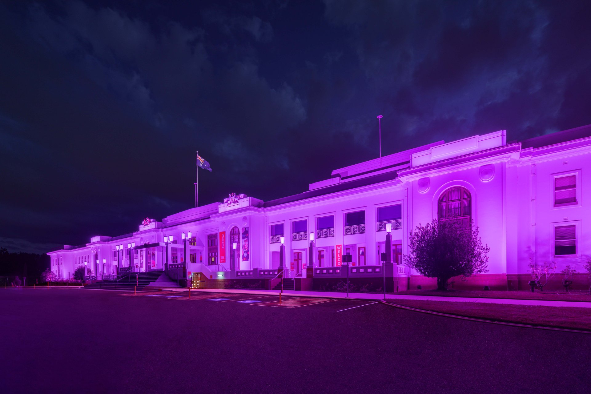 Old Parliament House illuminated in vibrant magenta-purple demonstrating WE-EF FLC200-CC projector series color-changing capability with RGBW and RGBA variants, stark white stripped classical facade by John Smith Murdoch serving as perfect canvas for projected light rendering color exceptionally well, precision wallwash lens optics leaving no imperfections visible on exterior walls, completed 2020 after years waiting for technology capable of realizing owners' vision for dynamic architectural lighting on National Heritage Register building
