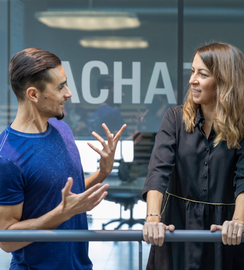 Two WE-EF colleagues in a friendly conversation at a railing in front of a glass-walled office