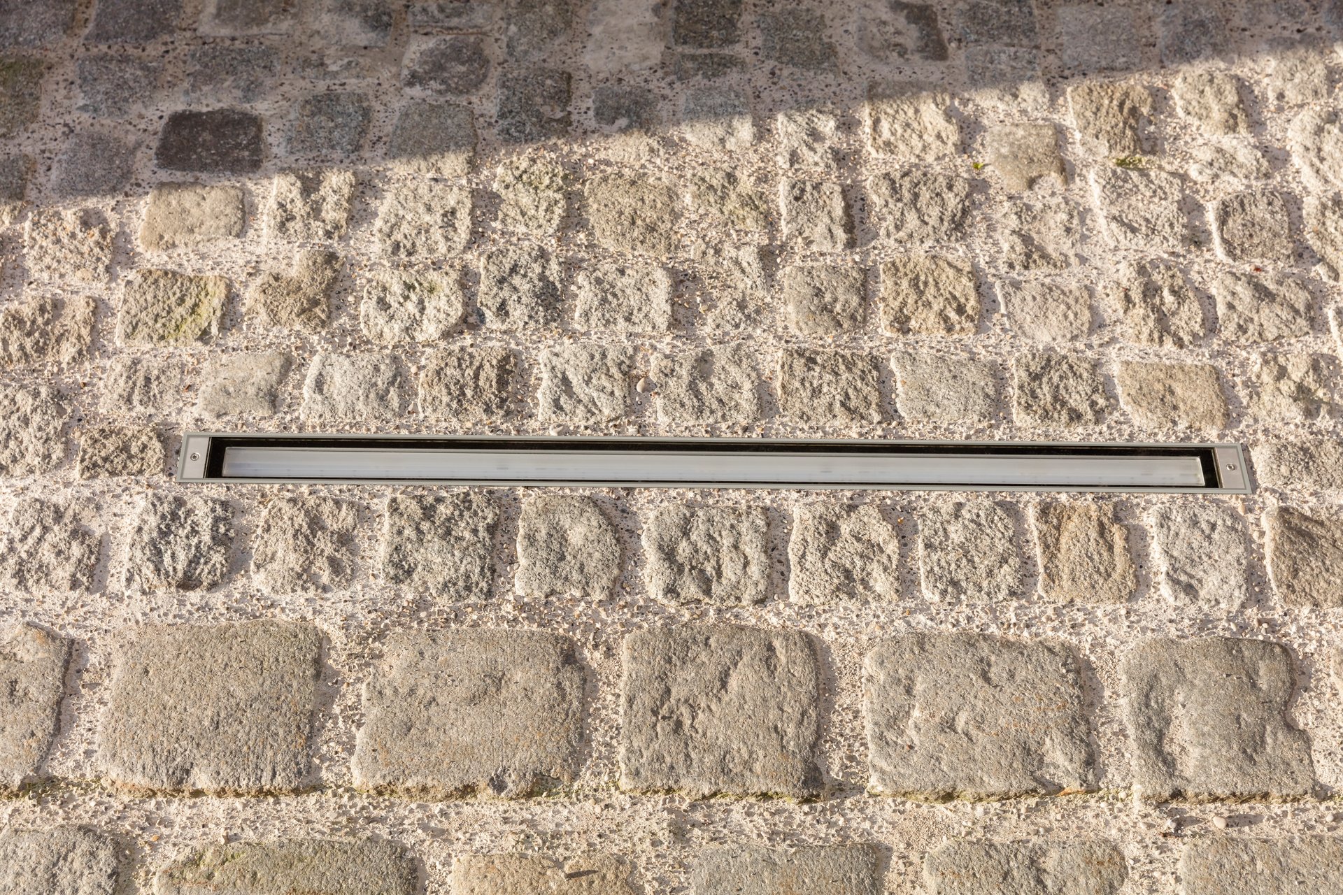 WE-EF ETV130 LED linear inground luminaire with asymmetric wallwash optics installed flush in historic cobblestone pavement at Bayertor, showing minimalist rectangular design that preserves medieval architectural character