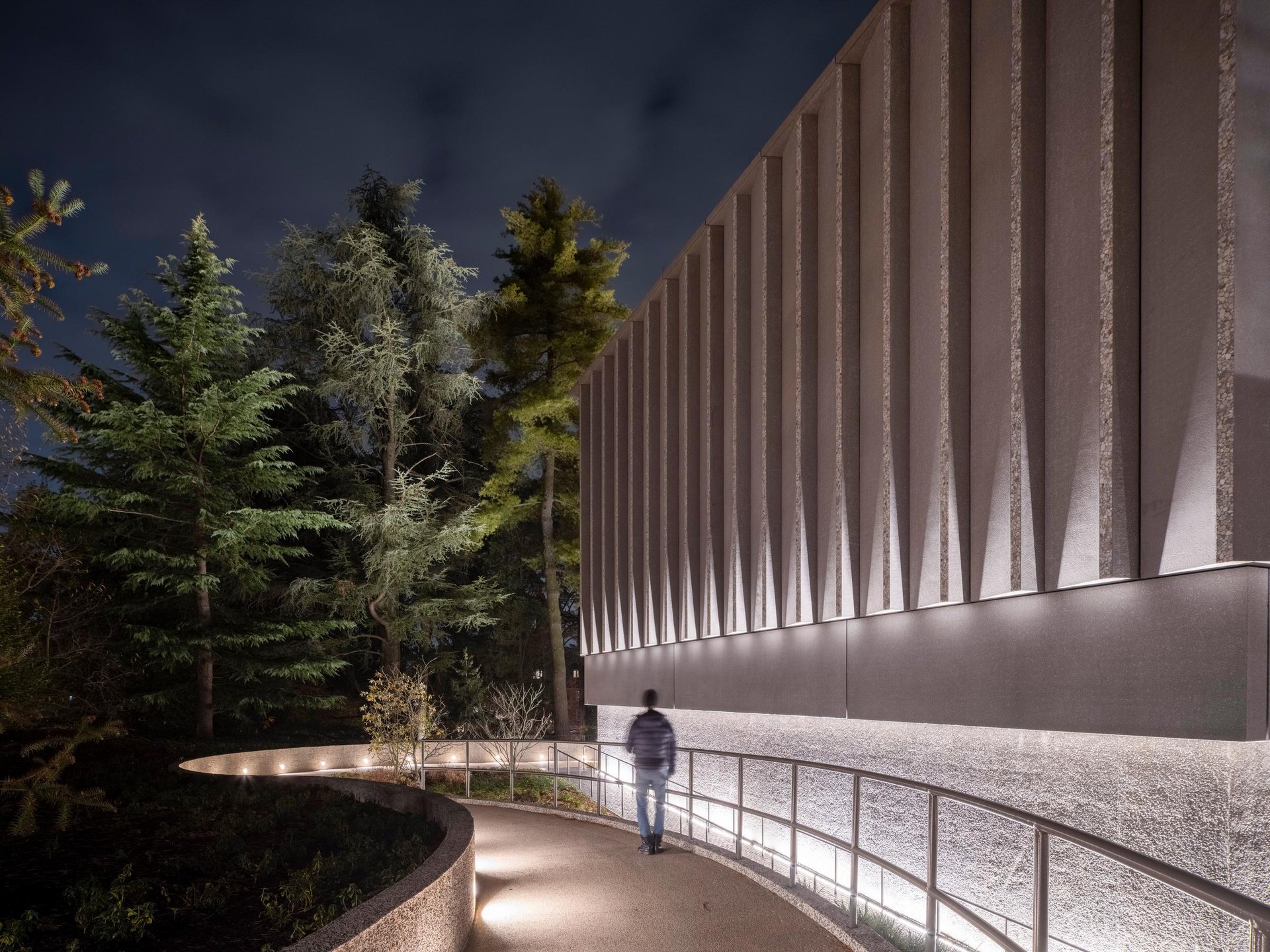 Man walking down lit pathway alongside building