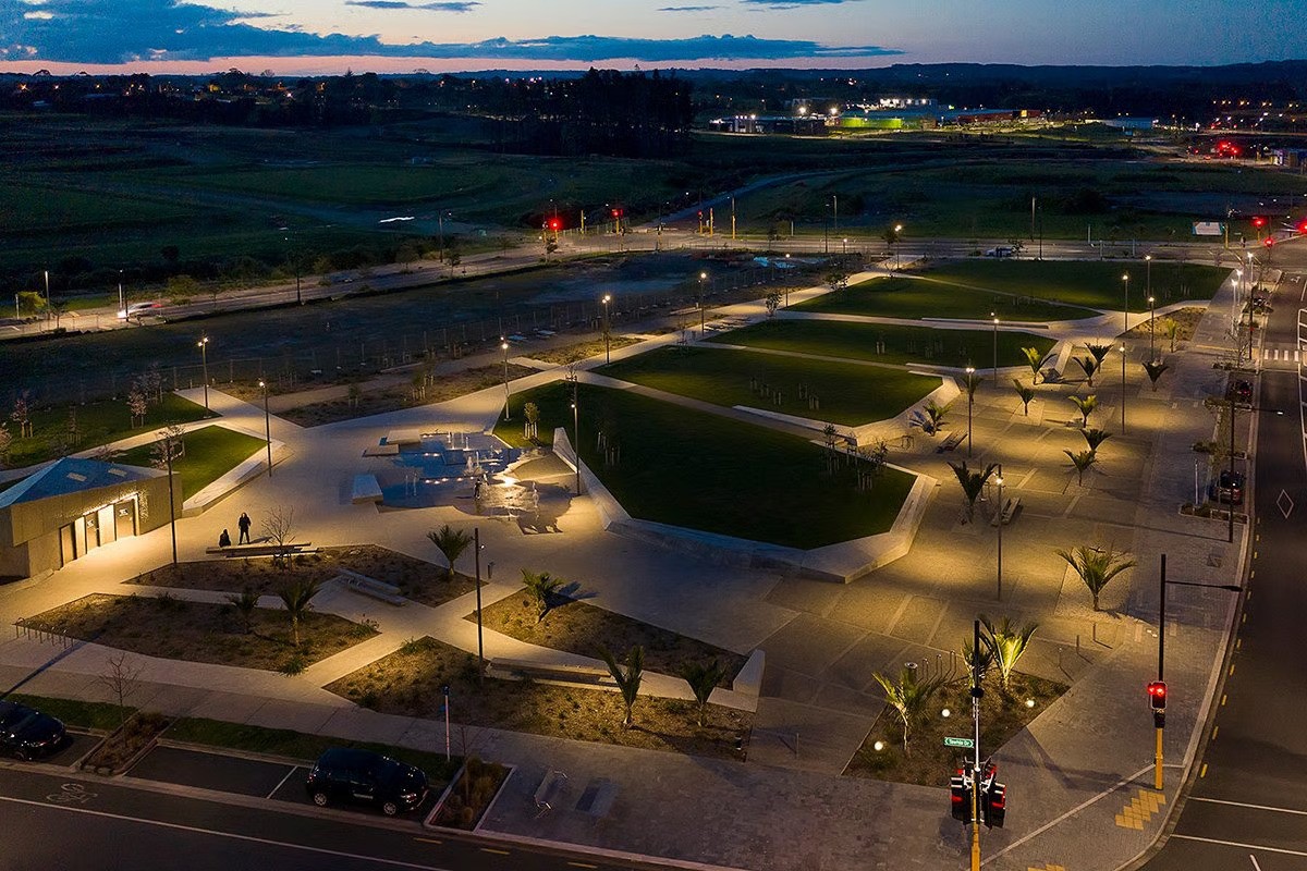 Te Hauāuru Park elevated view at twilight showing lower level promenade along street edge with shellfish motif inlays designed to accommodate markets, endemic New Zealand Nikau palm illuminated by WE-EF ETC330 inground luminaires, comprehensive lighting solution by MHL consultant Jayden Cocker using FLC121 projectors, DLG200 wall luminaires creating interactive recreational space for families and throughfare for workers, designed by Isthmus with WE-EF products chosen for longevity aesthetic appeal and positive experience