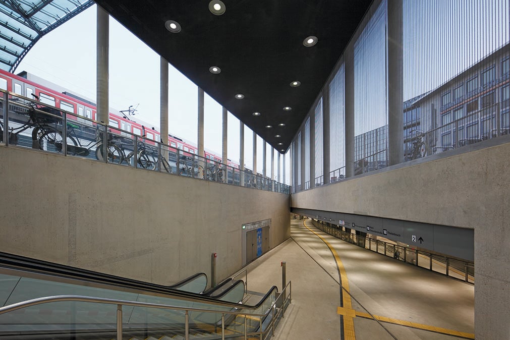 Escalator at Breslauer Platz underground station in Cologne with daylight entering through the glass facade, WE-EF recessed ceiling luminaires and a view of the illuminated underground platform