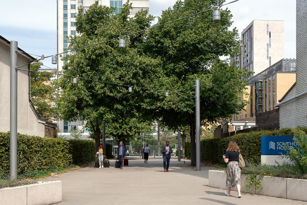 Southern House Croydon connecting path from George Street showing WE-EF DAC220 LED surface-mounted downlight on custom wire cable system stretched between poles with special mounting brackets developed by local WE-EF office for taut cable segments without standard sag, inspired by omnipresent overhead tramlines in Croydon cityscape, providing pedestrian access from nearby East Croydon railway station to rejuvenated 1960s 17-storey office complex in rapidly changing South London business district" Thumbnail 2 (Center-left - Pedestrian pathway daytime): "Southern House entrance pathway showing zigzag pattern of wire cables supporting WE-EF DAC220 LED downlights with symmetric wide-beam OLC One LED Concept optics for superior light and glare control, custom pendant luminaire solution designed by LUC Land Use Consultants London creating inviting easily-accessible pedestrian connection with new pathways, greenery, flooring and furniture as part of 2018 rejuvenation making building context attractive for working and living neighbourhood