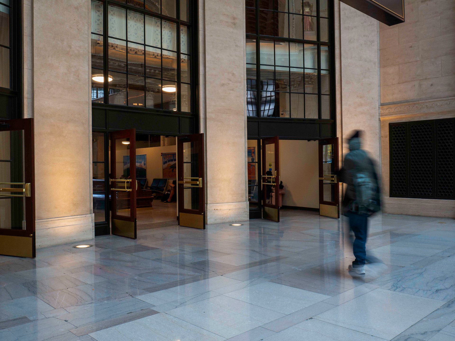 Man walking through double doors in a train station, ingrounds light the doors