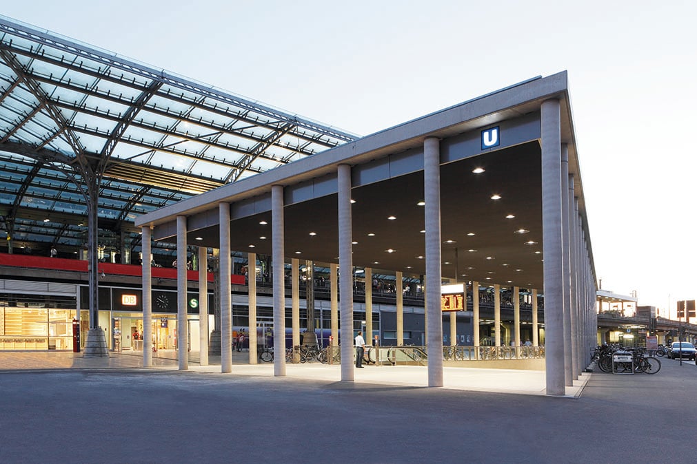 Exterior view of Breslauer Platz underground station in Cologne at dusk, with illuminated colonnade, WE-EF recessed ceiling luminaires and the glazed roof of Cologne Central Station in the background