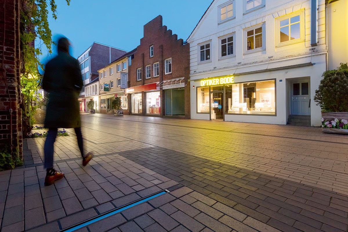 Elmshorn pedestrian zone at dusk with WE-EF ETV130 RGBW inground luminaires providing blue wayfinding light lines towards Krückau River Schleswig-Holstein