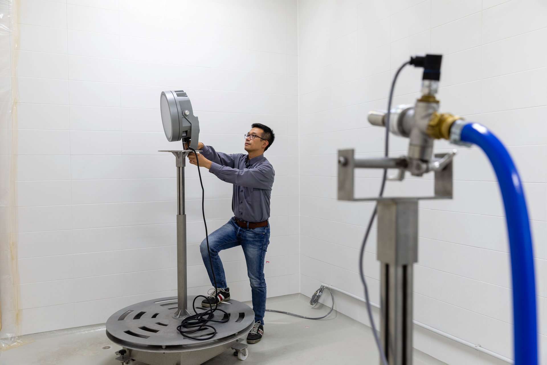 WE-EF engineer mounting a floodlight on a rotating test stand in a water-ingress test chamber
